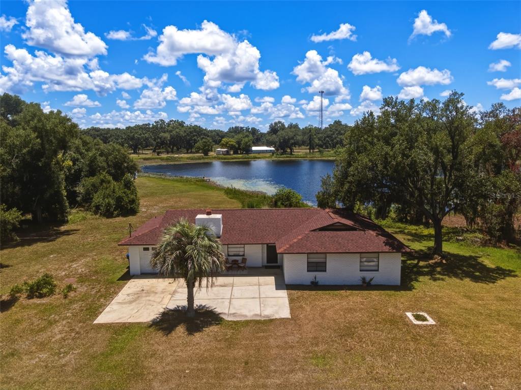 An aerial view shows a white brick house with a brown roof near a lake — 18208 STATE ROAD 52, LAND O LAKES, FL