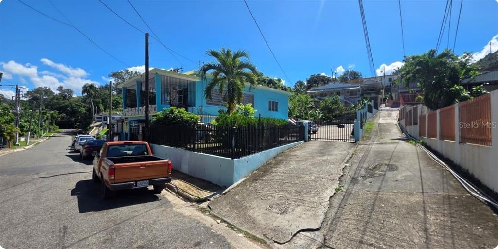 A blue house with a black metal fence and a concrete driveway sits on a corner — Carr PR-123 Km 78.9 BO HATO VIEJO, ARECIBO, PR