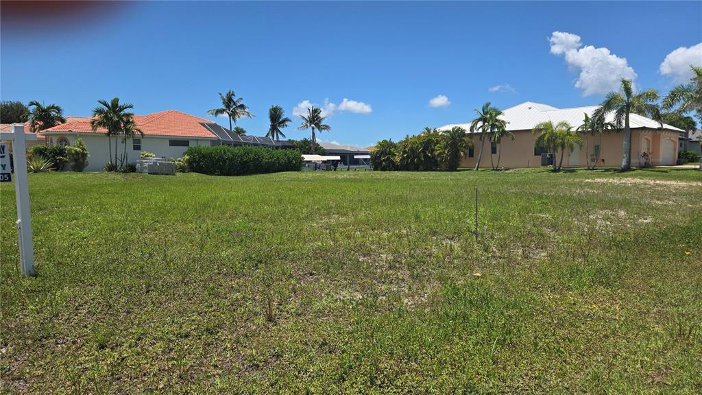 A vacant grassy residential lot is situated between two houses under a clear blue sky — 3600 NW 2ND TERRACE, CAPE CORAL, FL