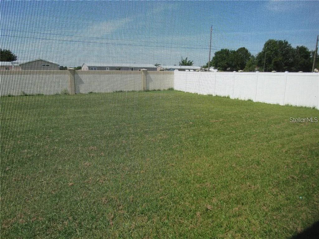 A grassy backyard is enclosed by a white vinyl fence and viewed through a screen — 8138 WILDER LOOP, LAKELAND, FL