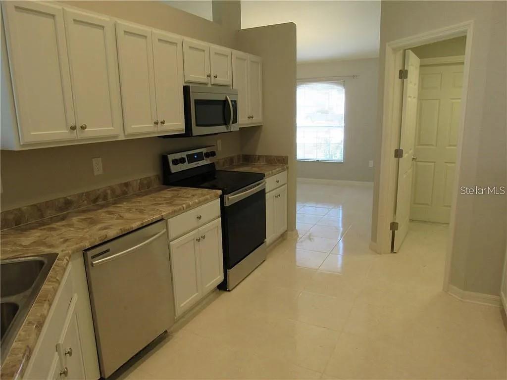 A kitchen features white cabinets, stainless steel appliances, and light-colored tile flooring — 8138 WILDER LOOP, LAKELAND, FL
