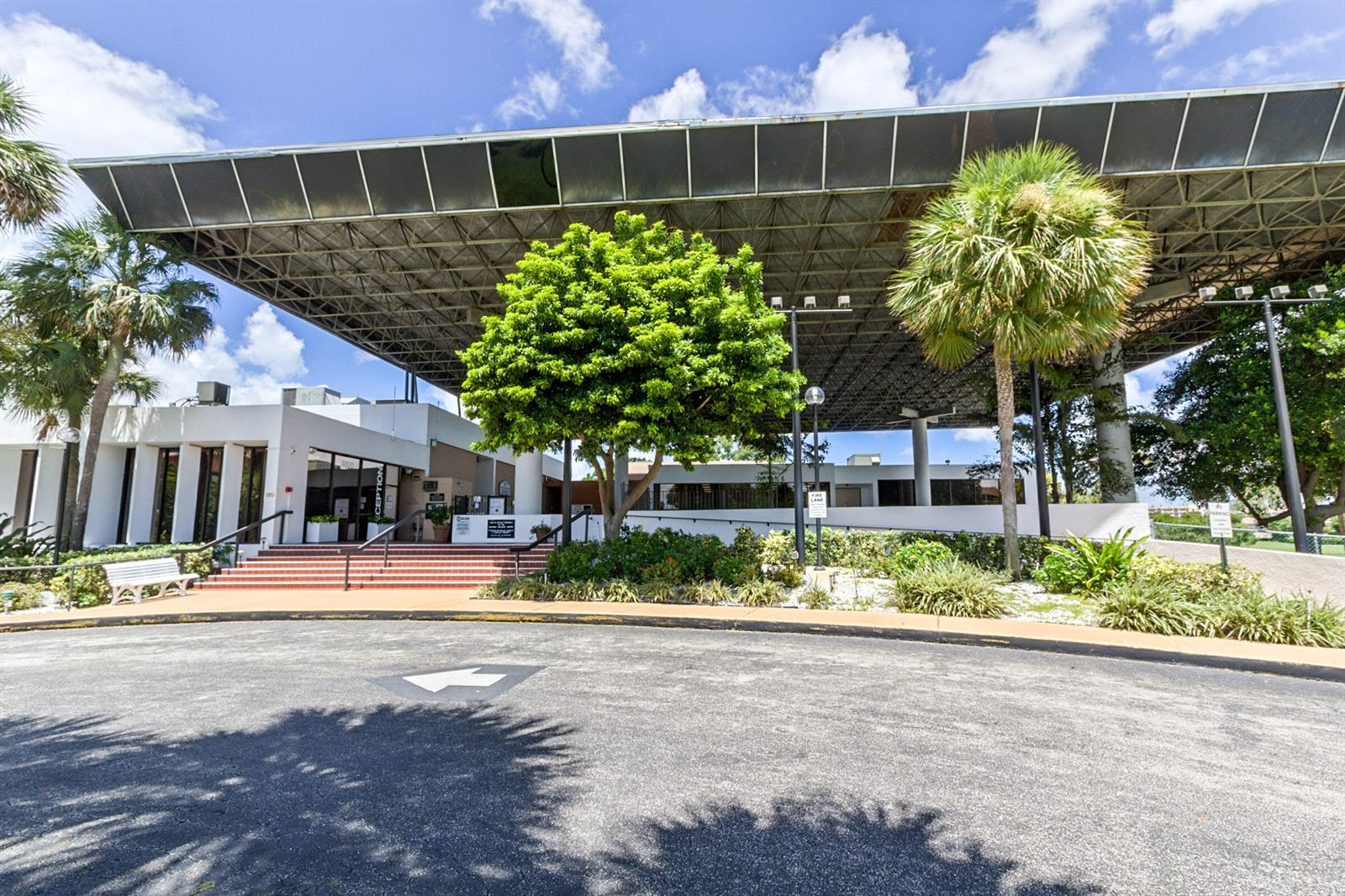 An exterior view of a modern building entrance with a large metal canopy and palm trees — 3671 Environ Boulevard # 169, Lauderhill FL 33319, LAUDERHILL, FL
