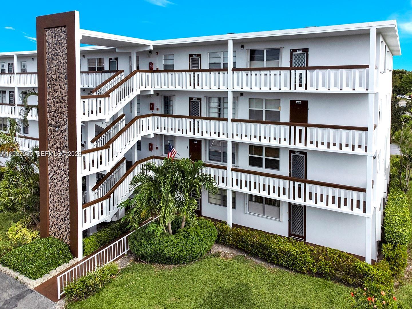 An exterior view of a three-story apartment building with white balconies and an outdoor staircase — 4052 E Harwood E # 4052, Deerfield Beach FL 33442, DEERFIELD BEACH, FL