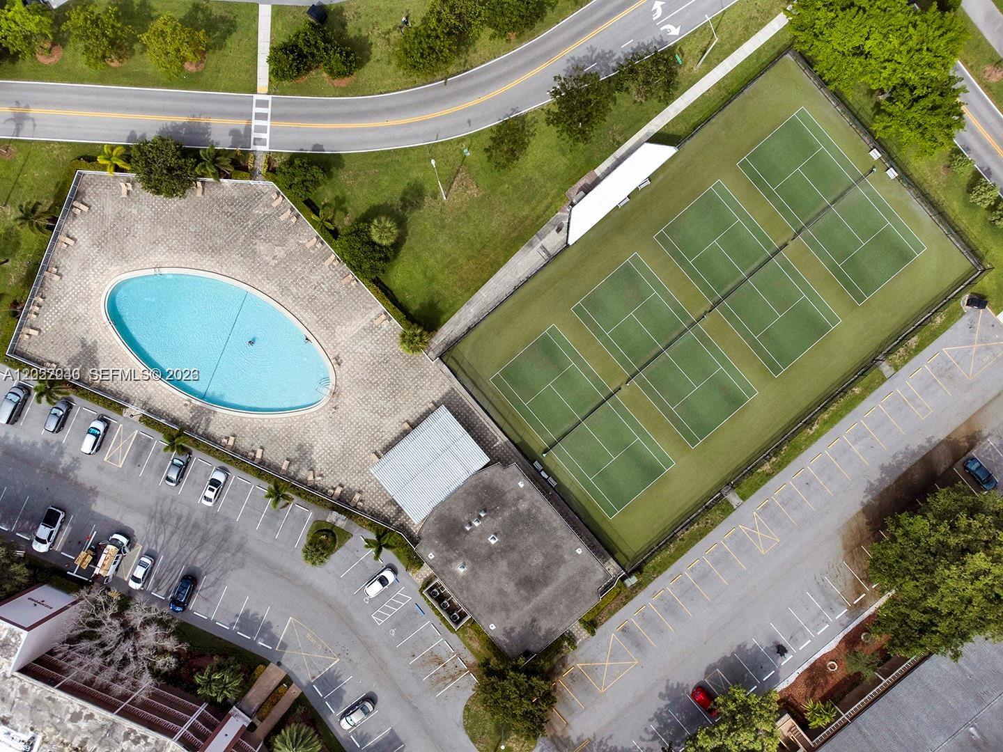 An aerial view shows a swimming pool, tennis courts, and parking lots near a road — 4052 E Harwood E # 4052, Deerfield Beach FL 33442, DEERFIELD BEACH, FL