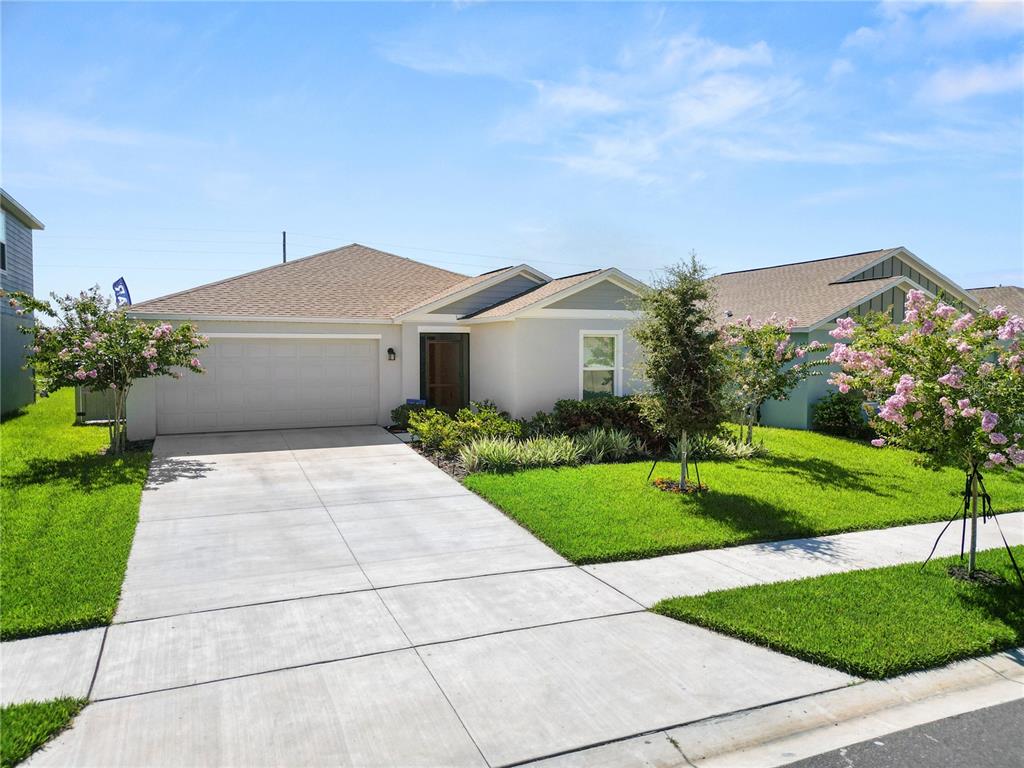 A single-story house with a two-car garage, concrete driveway, and blooming crepe myrtle trees — 2914 PENNACHIO DRIVE, LAKE WALES, FL