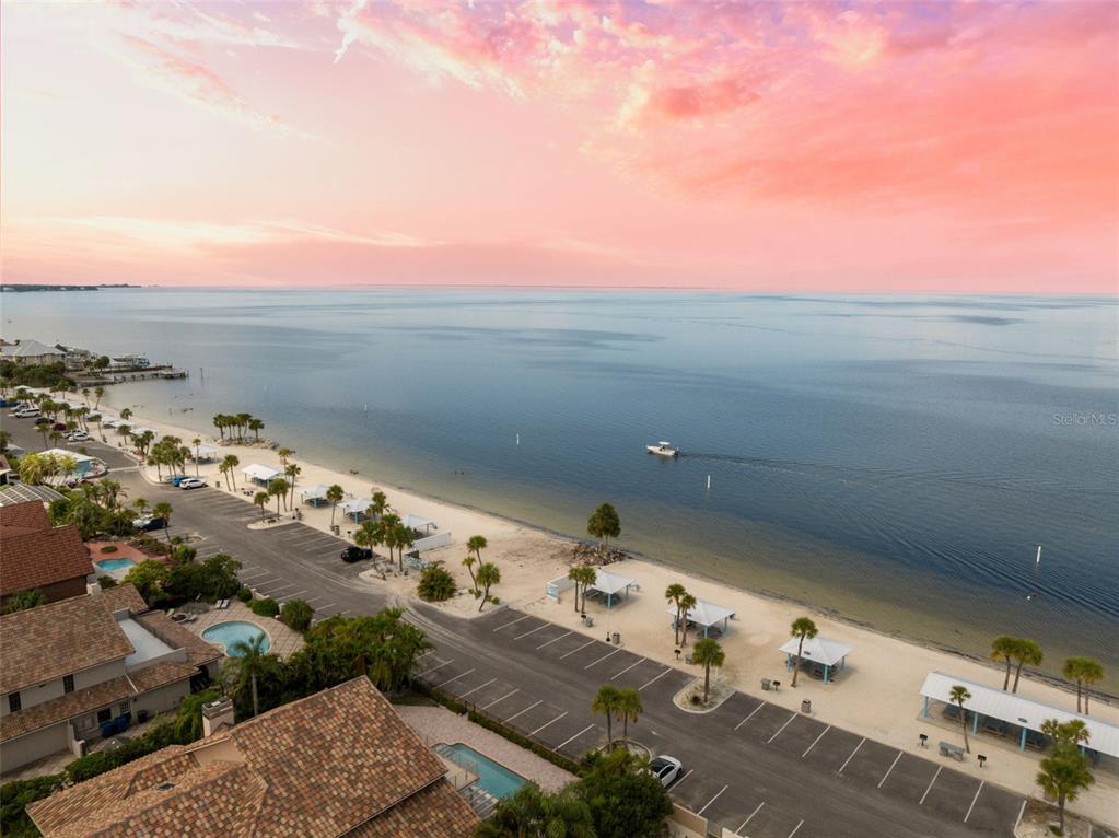An aerial view shows a beach with parking, palm trees, and a boat on water — 4926 FORECASTLE DRIVE, NEW PORT RICHEY, FL