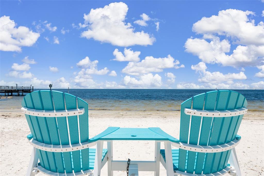 Two turquoise Adirondack chairs with a shared table face the ocean on a sandy beach — 4926 FORECASTLE DRIVE, NEW PORT RICHEY, FL