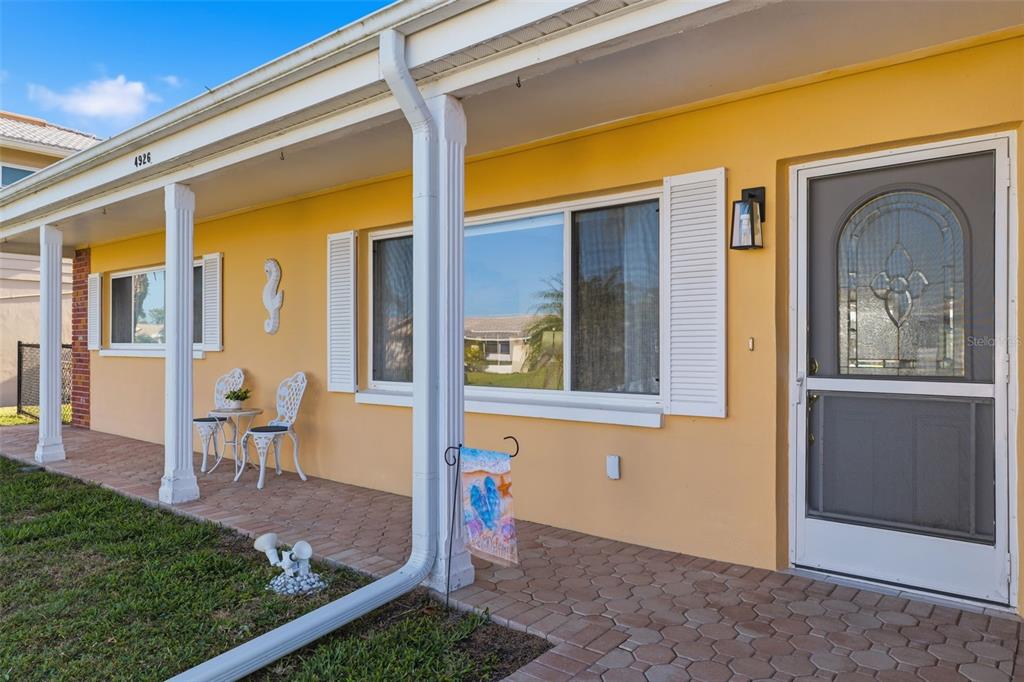 A yellow house exterior features a brick-paved porch, white columns, and a glass-paneled storm door — 4926 FORECASTLE DRIVE, NEW PORT RICHEY, FL