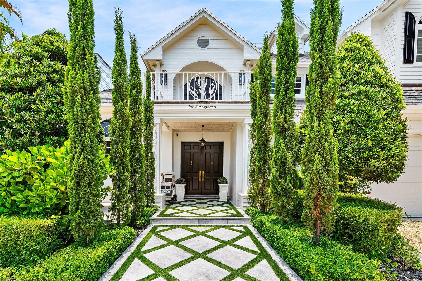 A white house exterior features a symmetrical walkway with geometric pavers and tall cypress trees — 477 NE Spanish Court, Boca Raton FL 33432, BOCA RATON, FL