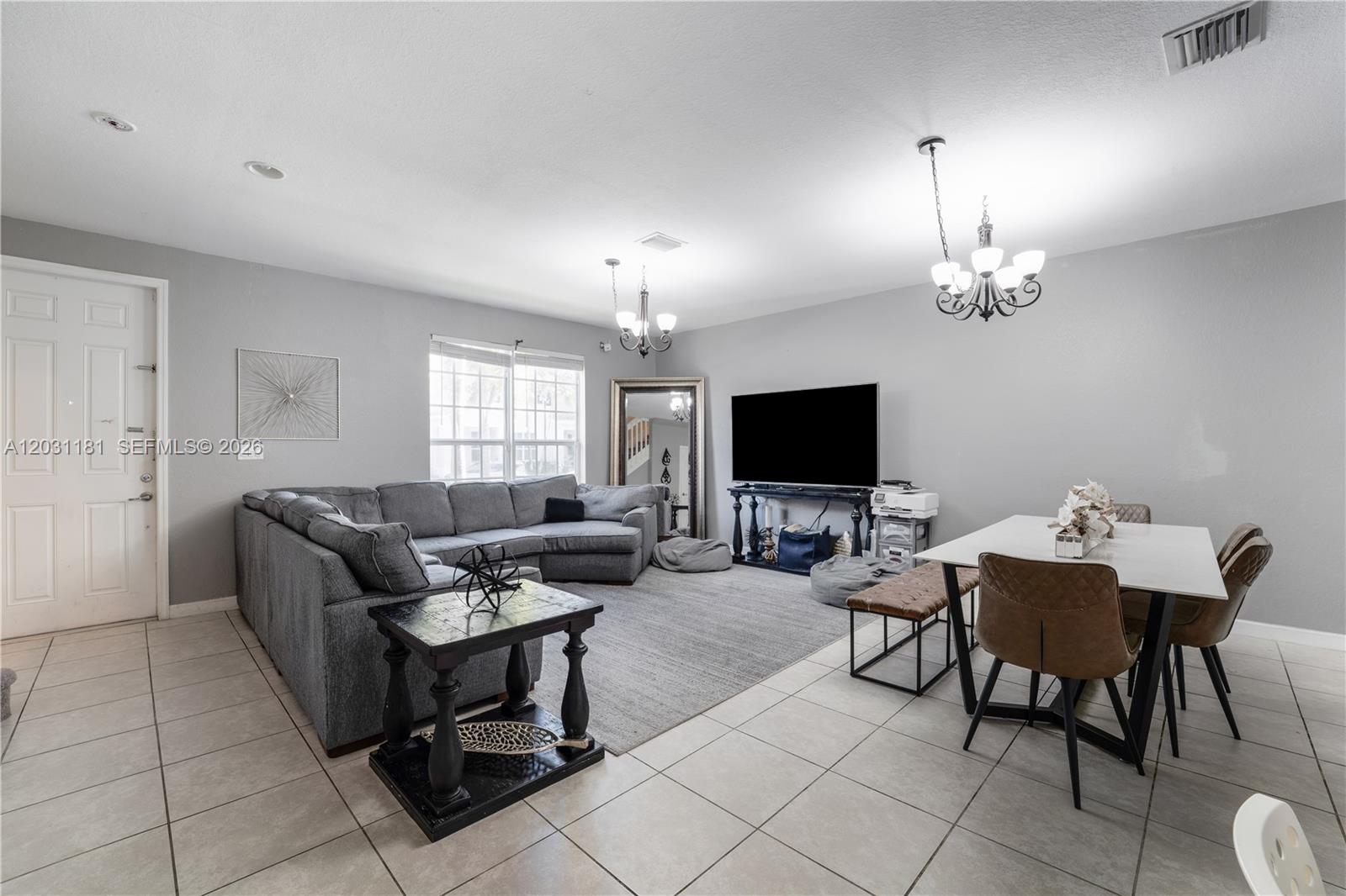 A living and dining area features gray walls, tile flooring, a sectional sofa, and chandeliers — 9360 SW 171st Ct, Miami FL 33196, MIAMI, FL