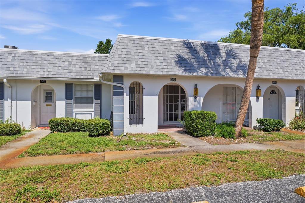 A row of single-story residential units features white stucco walls, arched entryways, and gray shingles — 4209 TOUCHTON PLACE, NEW PORT RICHEY, FL