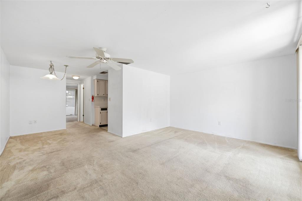 A spacious living room with beige carpet, white walls, a ceiling fan, and a dining area — 4209 TOUCHTON PLACE, NEW PORT RICHEY, FL