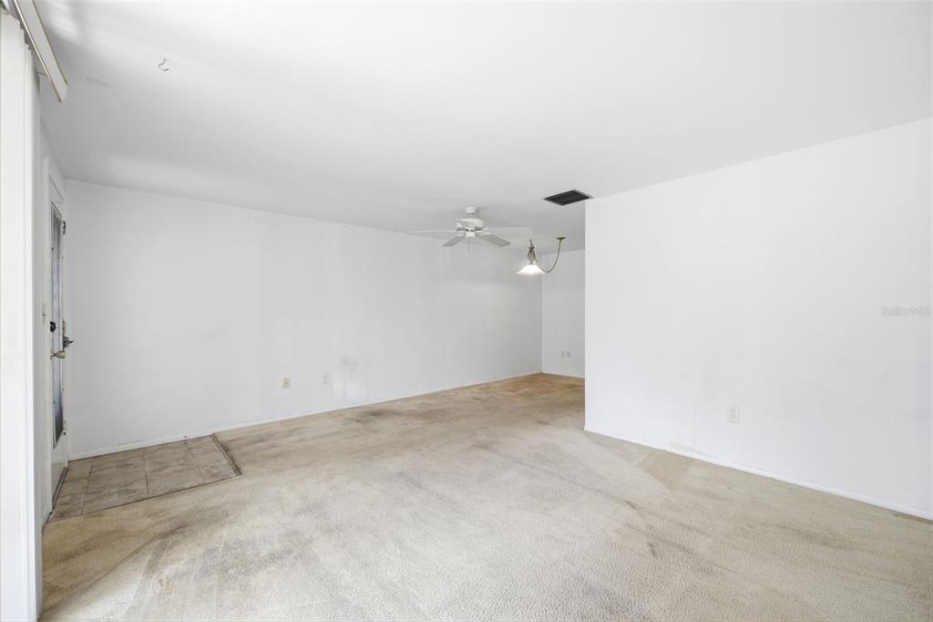 An empty living room with white walls, beige carpeting, a ceiling fan, and a light fixture — 4209 TOUCHTON PLACE, NEW PORT RICHEY, FL