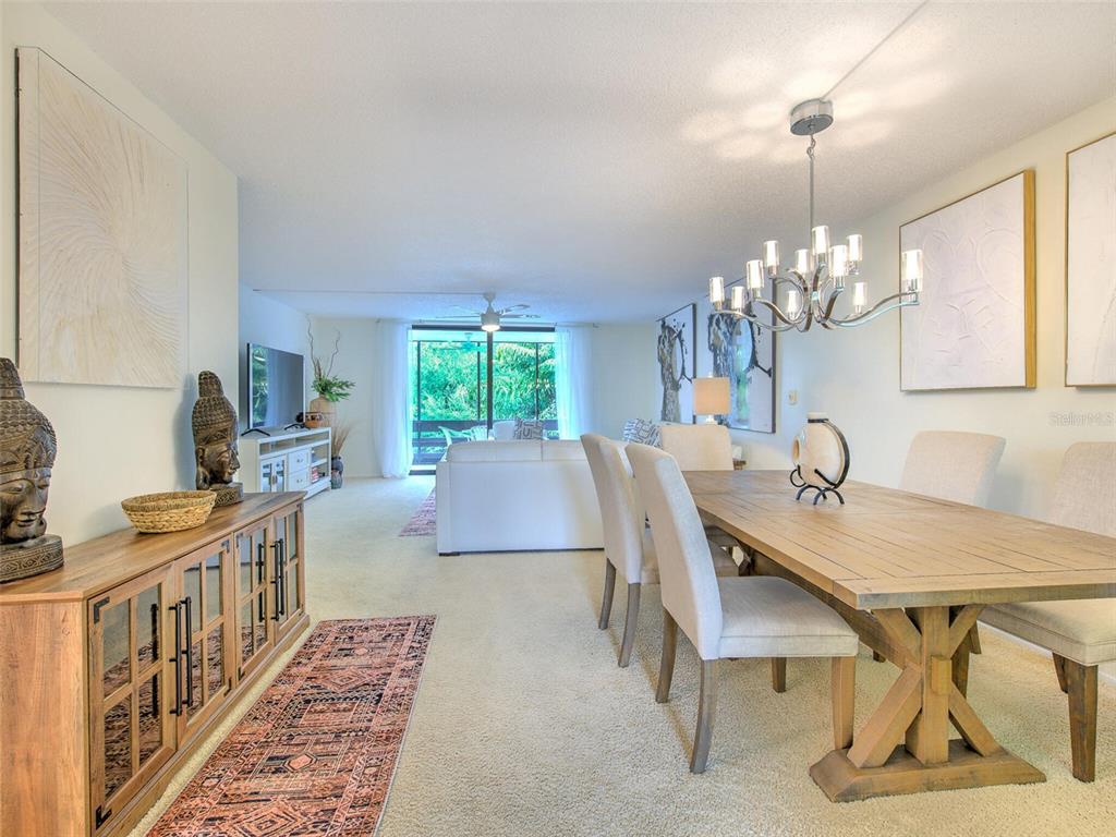 A dining area with a wooden table and chandelier opens into a living room — 833 BAYPORT WAY UNIT 833, LONGBOAT KEY, FL