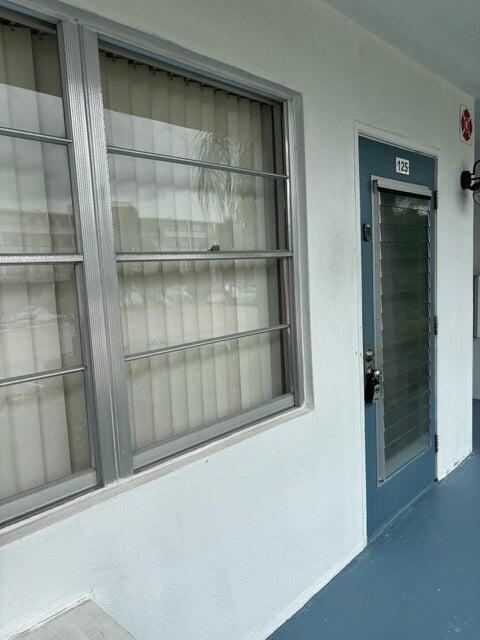 A white exterior wall features a large window with vertical blinds and a blue door — 125 Westbury Circle # G, Deerfield Beach FL 33442, DEERFIELD BEACH, FL