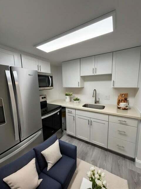A small kitchen features white cabinets, stainless steel appliances, and a blue sofa in front — 125 Westbury Circle # G, Deerfield Beach FL 33442, DEERFIELD BEACH, FL
