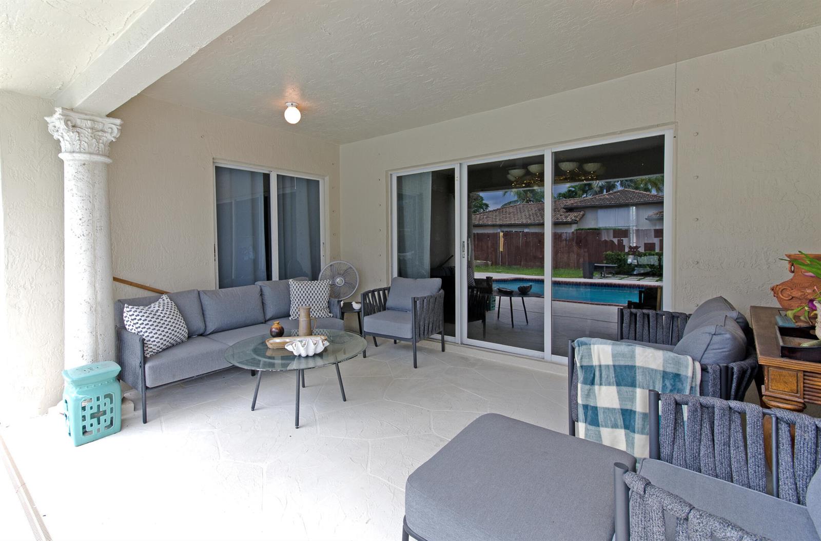 A covered patio features gray outdoor furniture, a glass coffee table, and a pool view — 18324 SW 149th Place, Miami FL 33187, MIAMI, FL