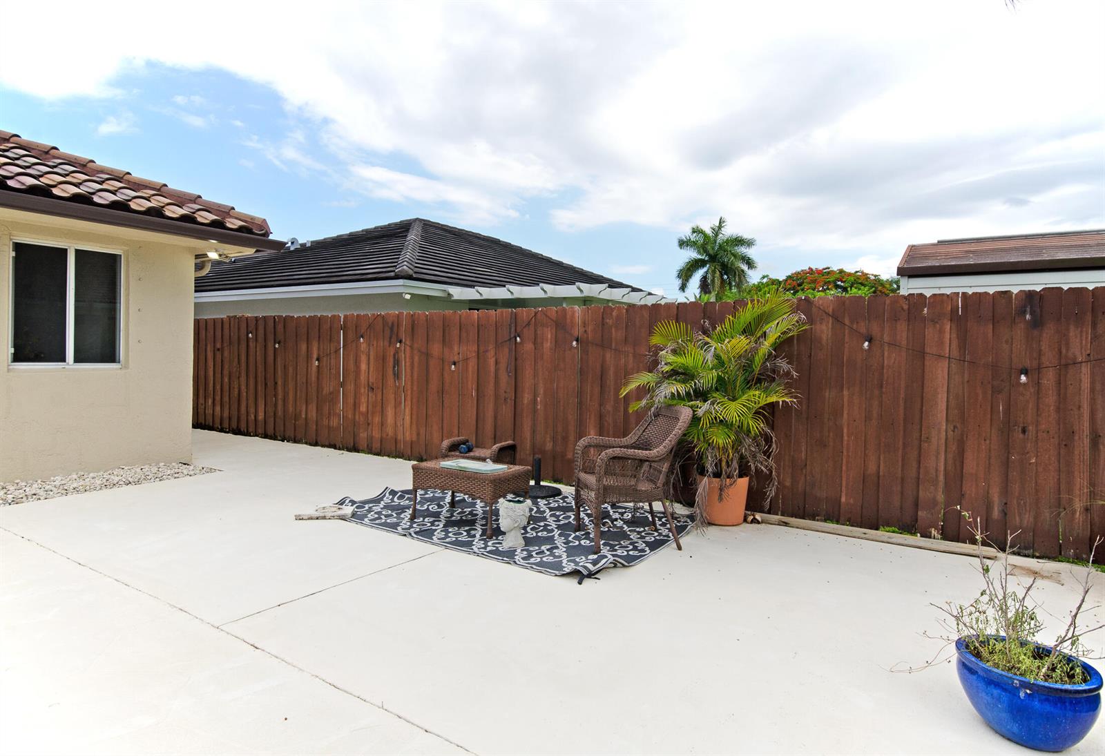 A concrete patio features a small wicker furniture set, a potted palm, and a wooden fence — 18324 SW 149th Place, Miami FL 33187, MIAMI, FL
