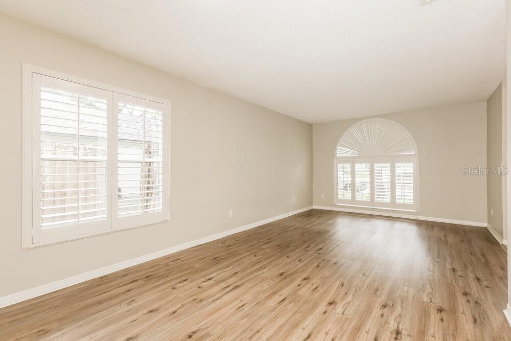 An empty room features light-colored walls, wood-look flooring, and two windows with white shutters — 2321 LYNCREST COURT, VALRICO, FL