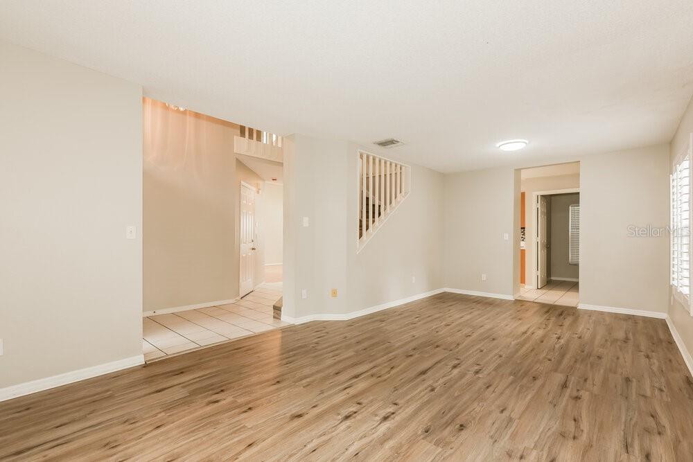 An empty room with light wood-look flooring, beige walls, and a staircase with white railings — 2321 LYNCREST COURT, VALRICO, FL