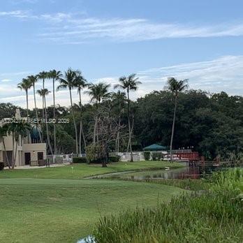 A view of a grassy golf course with palm trees and a house in the background — 9495 Evergreen Pl # 102, Davie FL 33324, DAVIE, FL