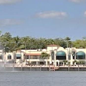 A waterfront building with arched windows and a fountain sits along a grassy shoreline — 9495 Evergreen Pl # 102, Davie FL 33324, DAVIE, FL