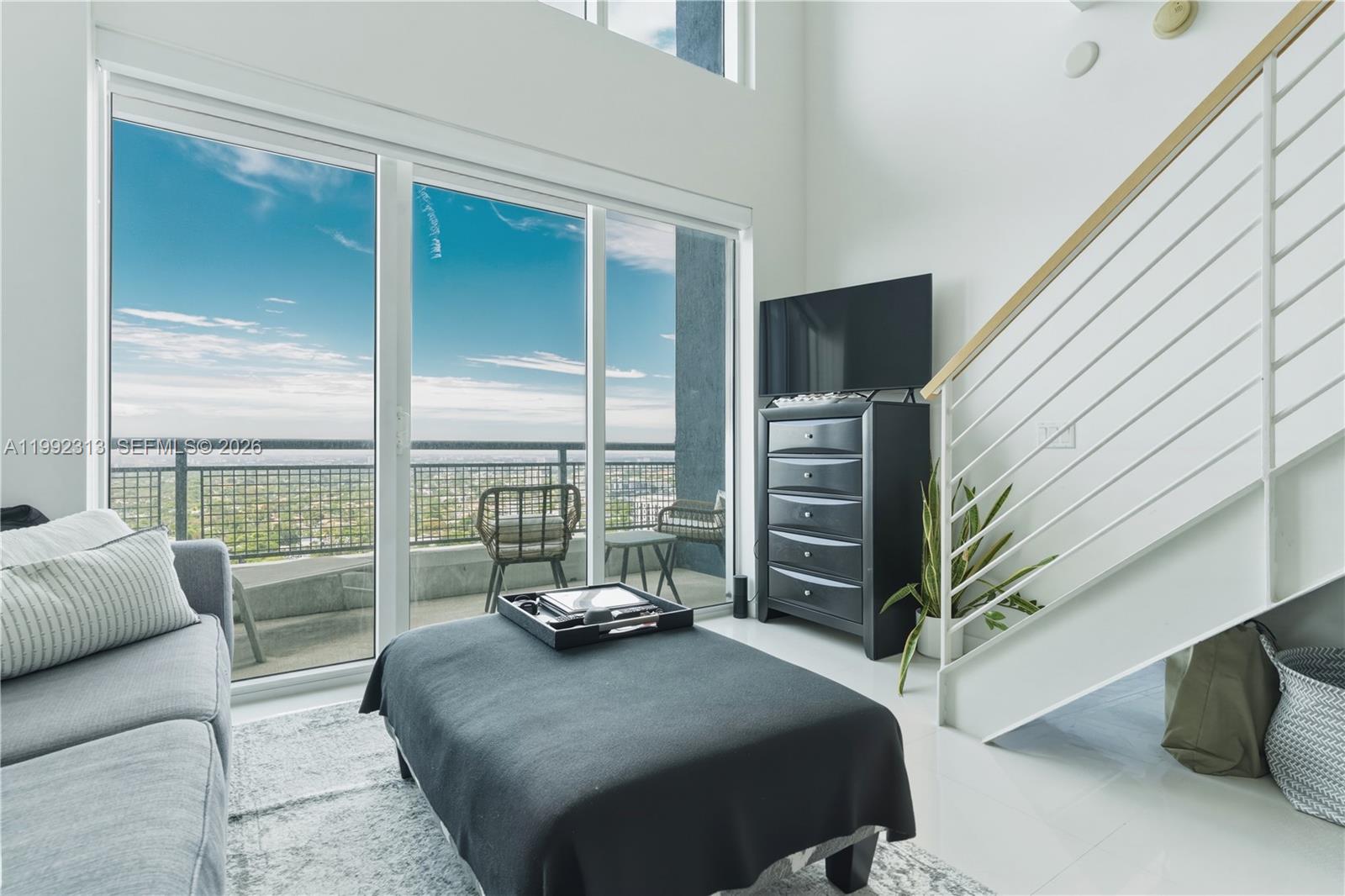 A modern living room features a high ceiling, large glass doors, and a balcony view — 60 SW 13th St # 2805, Miami FL 33130, MIAMI, FL