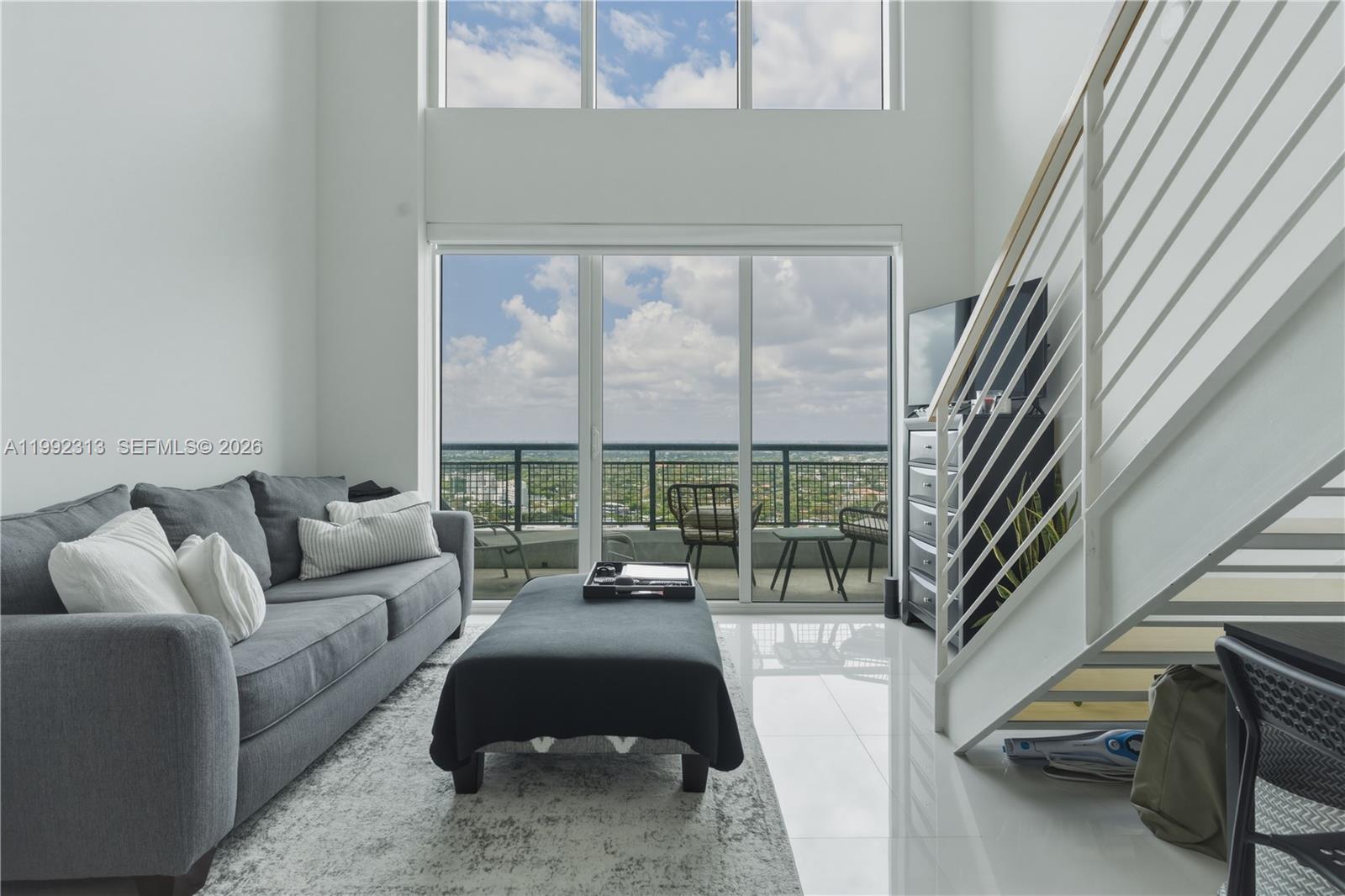 A modern living room features a gray sofa, white tile floors, and floor-to-ceiling windows — 60 SW 13th St # 2805, Miami FL 33130, MIAMI, FL