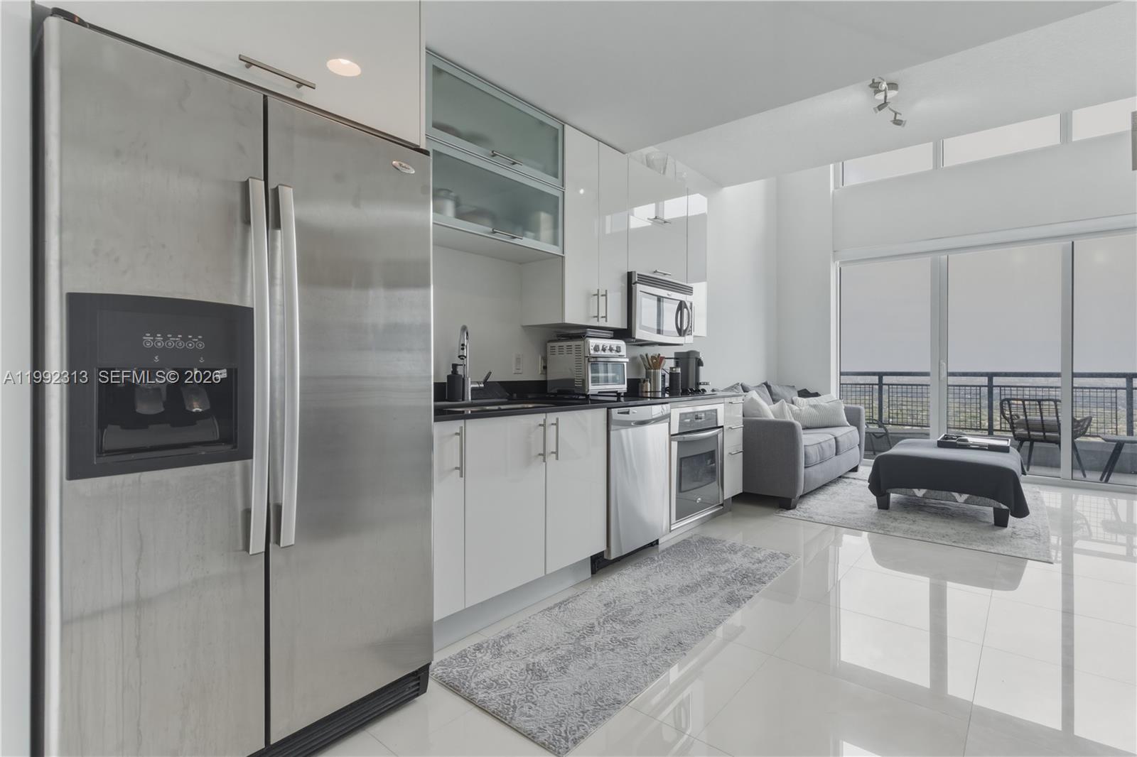 A modern kitchen with stainless steel appliances and white cabinetry opens into a living area — 60 SW 13th St # 2805, Miami FL 33130, MIAMI, FL