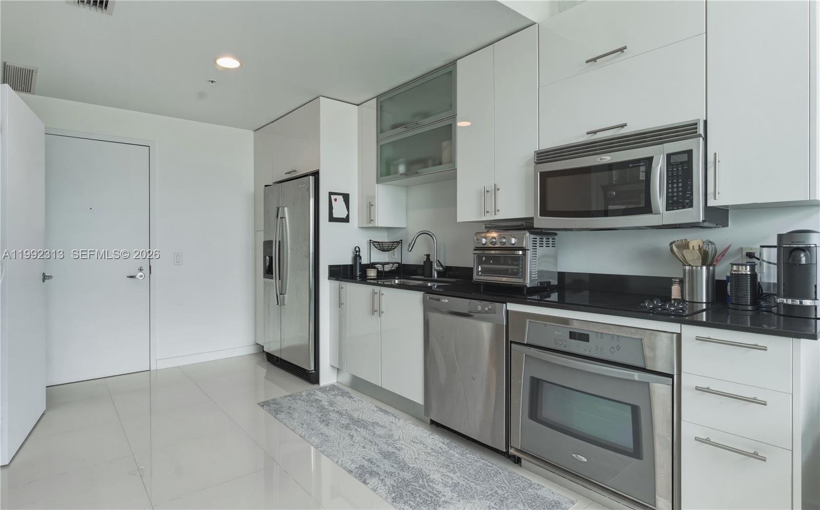 A modern kitchen features white cabinetry, stainless steel appliances, and black countertops — 60 SW 13th St # 2805, Miami FL 33130, MIAMI, FL