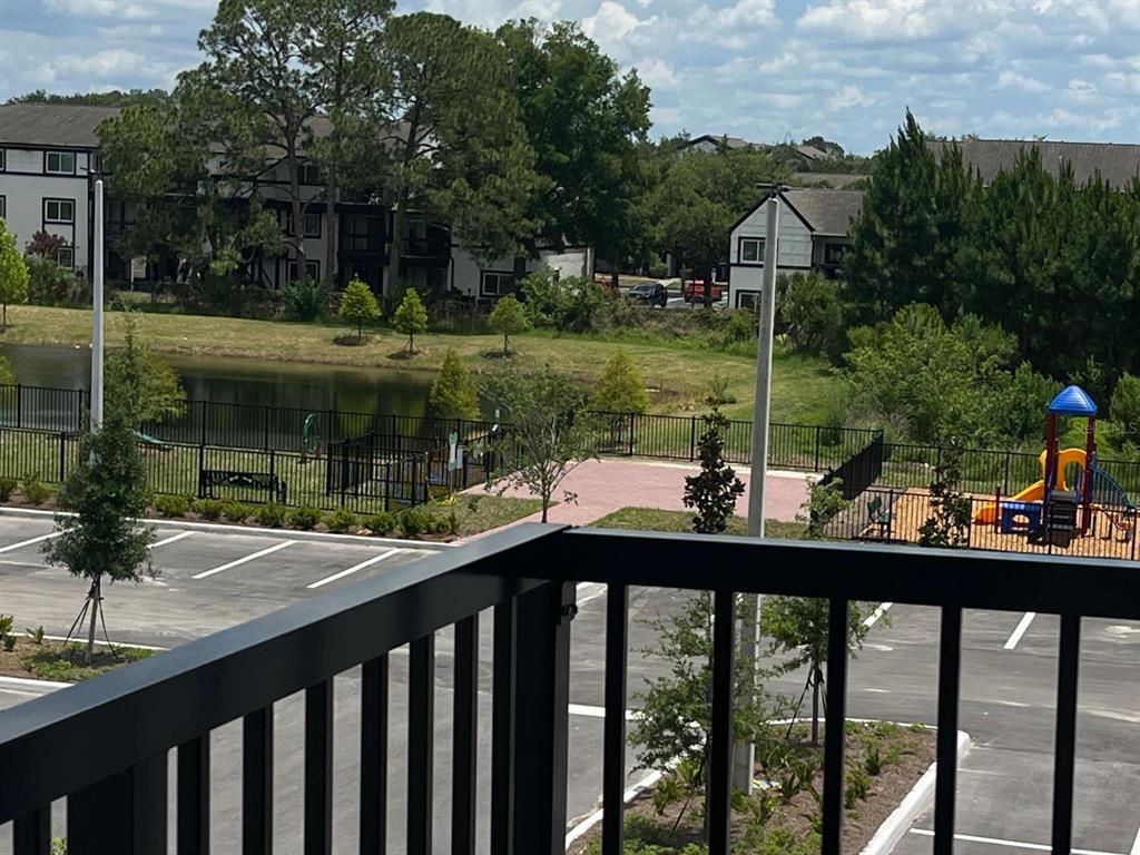 An elevated view from a balcony overlooks a parking lot, a pond, and a playground — 5579 MILLENIA PARK BOULEVARD UNIT 318, ORLANDO, FL