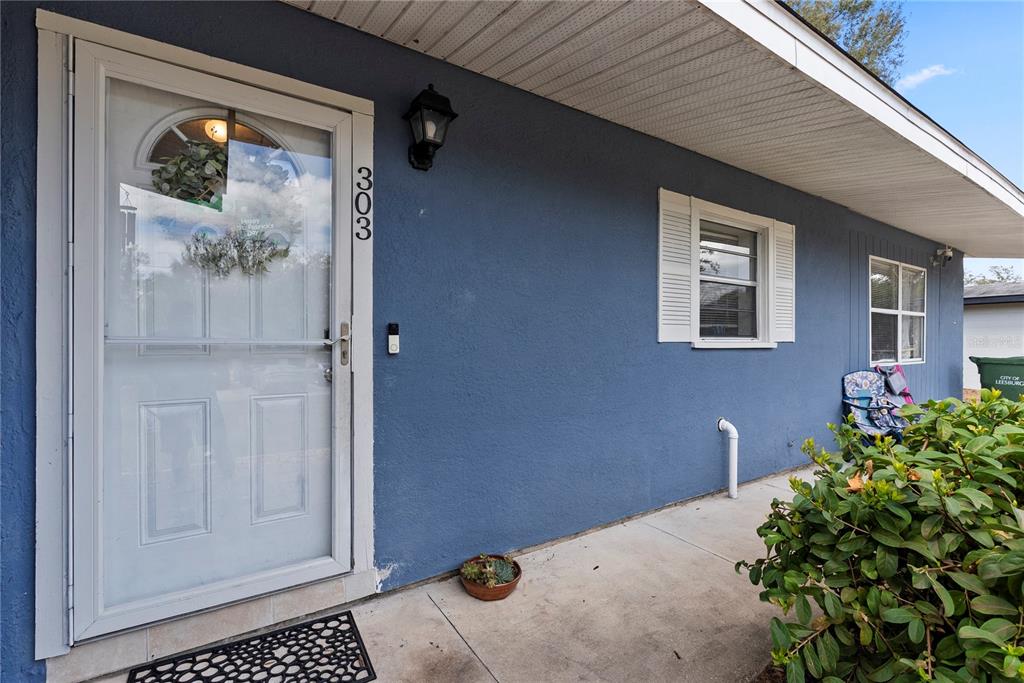 A blue exterior wall features a front door, a window with shutters, and a porch — 303 LOUIS STREET, LEESBURG, FL