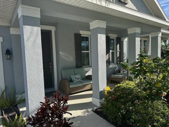 A covered front porch features gray stucco columns, a wicker loveseat, and dark shutters — 5262 ASHER COURT, SARASOTA, FL