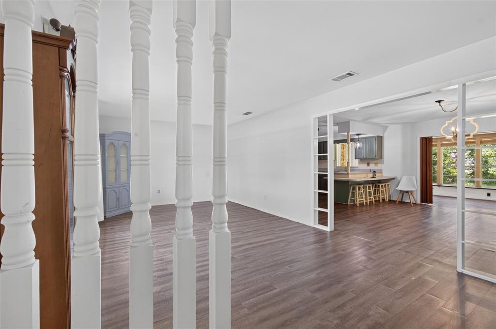 A view through white wooden spindles into an open-concept living area with wood-look flooring — 1321 NW 31ST DRIVE, GAINESVILLE, FL