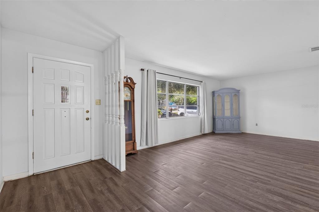 A living room features white walls, wood-look flooring, a front door, and a grandfather clock — 1321 NW 31ST DRIVE, GAINESVILLE, FL
