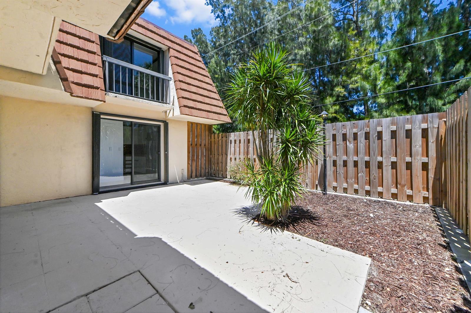 A concrete patio sits beside a house with a brown mansard roof and wooden fence — 825 Center Street # 12a, Jupiter FL 33458, JUPITER, FL