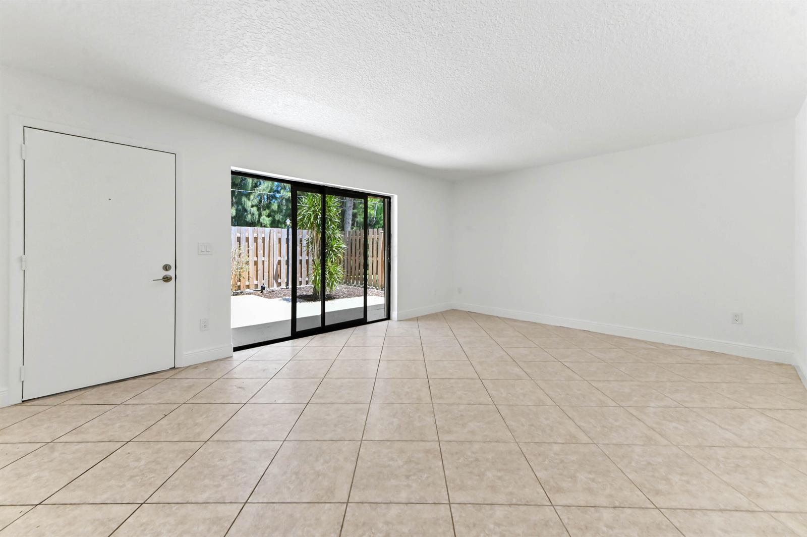 An empty room with white walls, beige tile flooring, and a sliding glass door — 825 Center Street # 12a, Jupiter FL 33458, JUPITER, FL