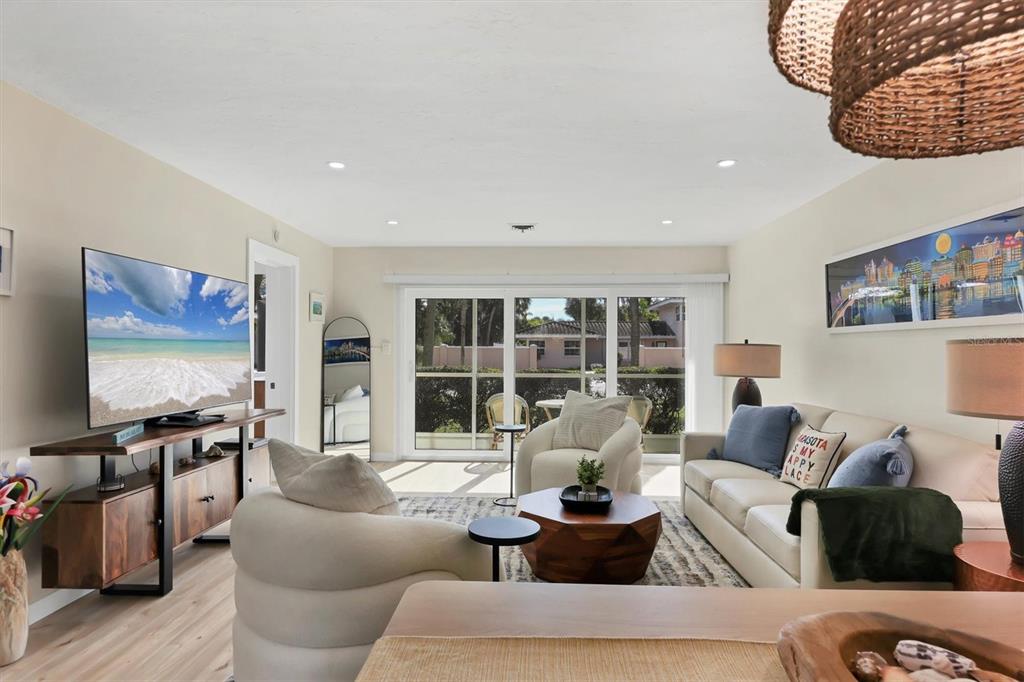 A bright living room features a television, white sofa, armchairs, and sliding glass patio doors — 500 S WASHINGTON DRIVE UNIT 5A, SARASOTA, FL