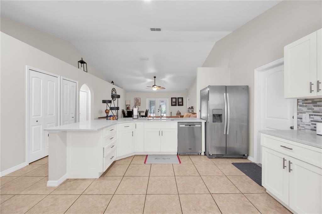A kitchen with white cabinets, stainless steel appliances, and tile flooring opens to a living area — 2980 BEAL ST STREET, DELTONA, FL