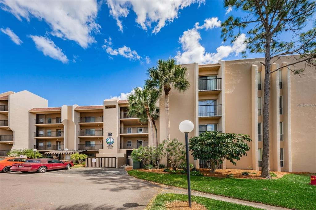 A multi-story apartment building with tan stucco walls and balconies stands under a blue sky — 90 S HIGHLAND AVENUE UNIT 214, TARPON SPRINGS, FL