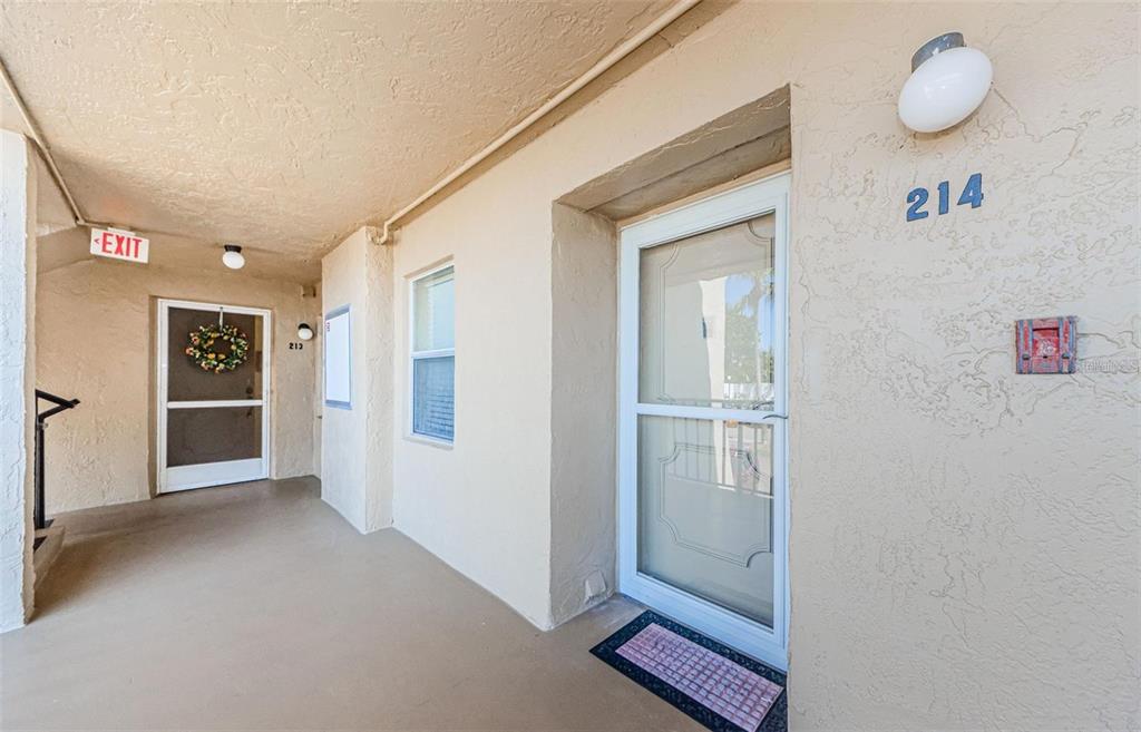 An exterior hallway shows two apartment doors with screen doors and unit numbers — 90 S HIGHLAND AVENUE UNIT 214, TARPON SPRINGS, FL