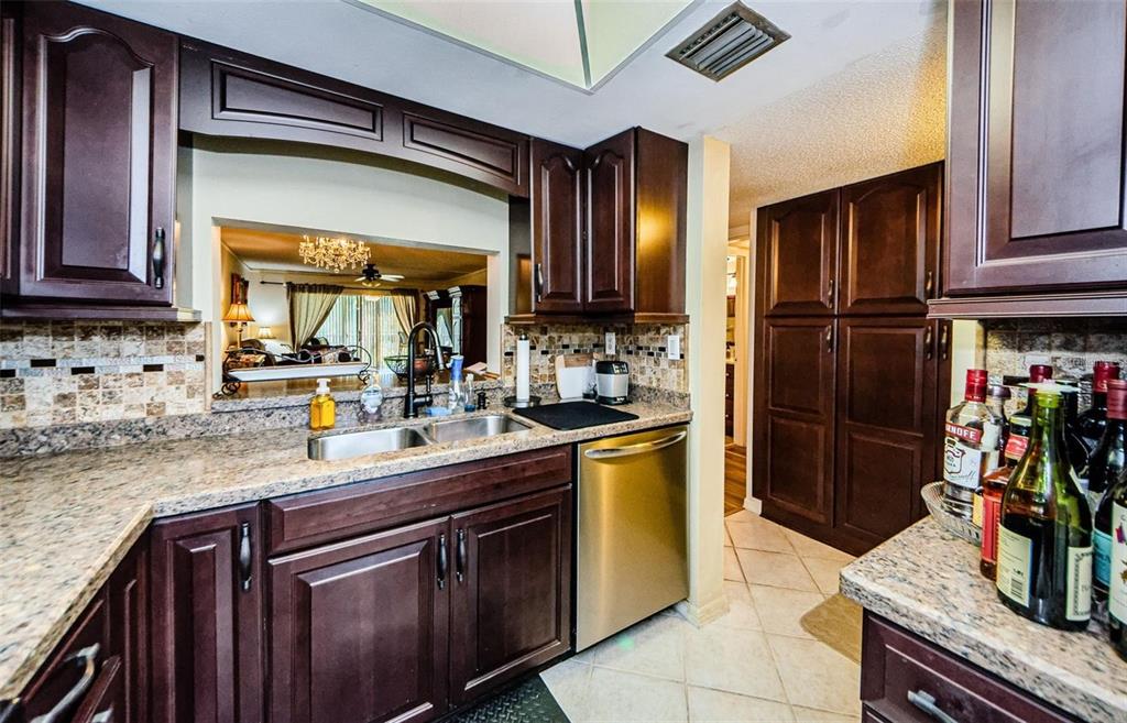 A kitchen features dark wood cabinets, granite countertops, a stainless steel dishwasher, and a pass-through — 90 S HIGHLAND AVENUE UNIT 214, TARPON SPRINGS, FL
