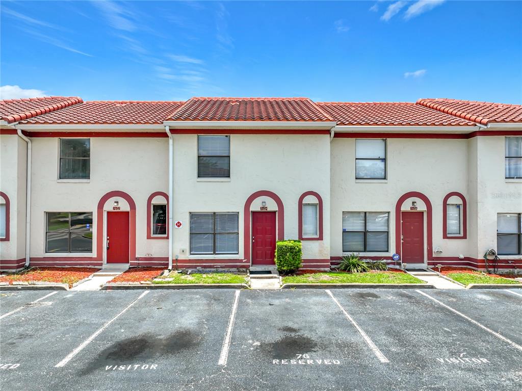 A row of two-story townhouses with red doors, arched entryways, and a paved parking lot — 1604 LITTLE FALLS CIRCLE UNIT 76, ORLANDO, FL
