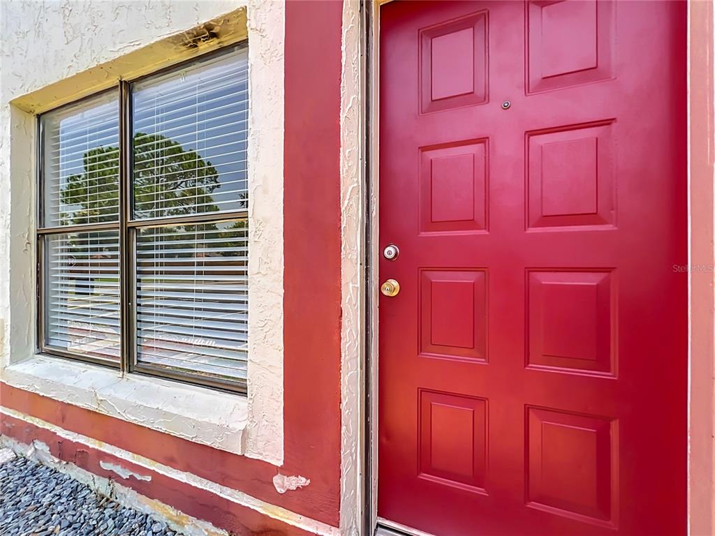 A red front door sits next to a window with white blinds on a building exterior — 1604 LITTLE FALLS CIRCLE UNIT 76, ORLANDO, FL