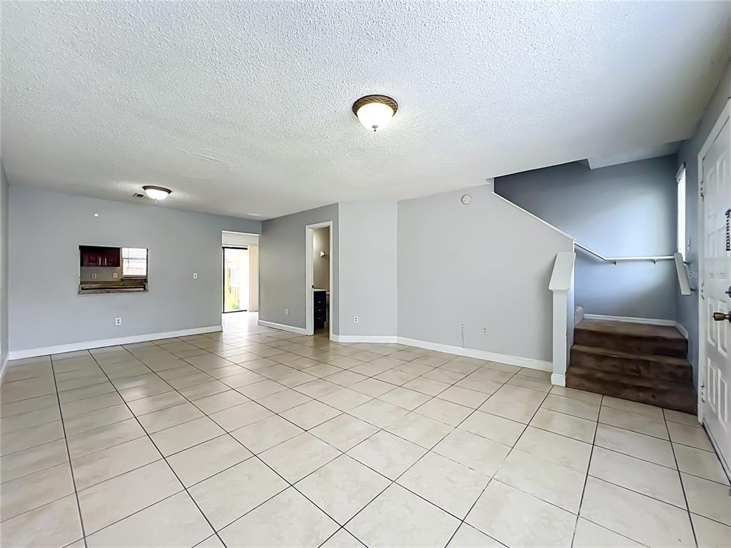 An open living area features light-colored tile flooring, gray walls, and a carpeted staircase — 1604 LITTLE FALLS CIRCLE UNIT 76, ORLANDO, FL