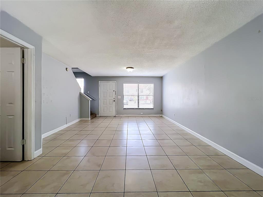 An empty living room features light gray walls, beige tile flooring, and a front door — 1604 LITTLE FALLS CIRCLE UNIT 76, ORLANDO, FL