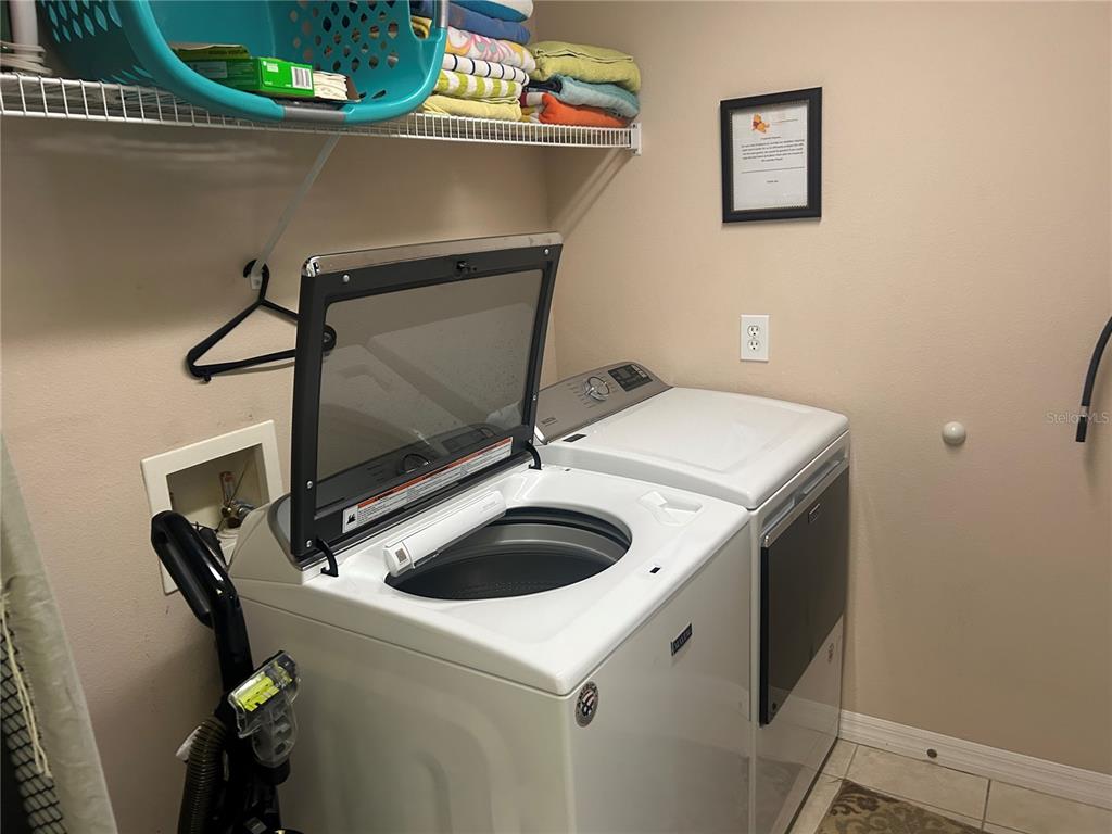 A laundry room features a top-loading washing machine, a dryer, and overhead wire shelving — 190 MINNIEHAHA CIRCLE, HAINES CITY, FL