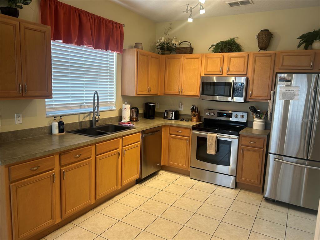 A kitchen features light wood cabinets, stainless steel appliances, and a dark sink — 190 MINNIEHAHA CIRCLE, HAINES CITY, FL