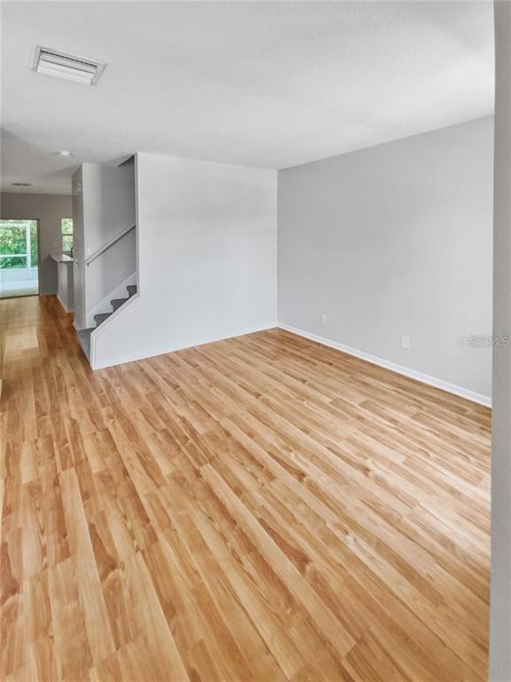 An empty living room features light wood-look flooring, gray walls, and a staircase — 30205 SWINFORD LANE, WESLEY CHAPEL, FL