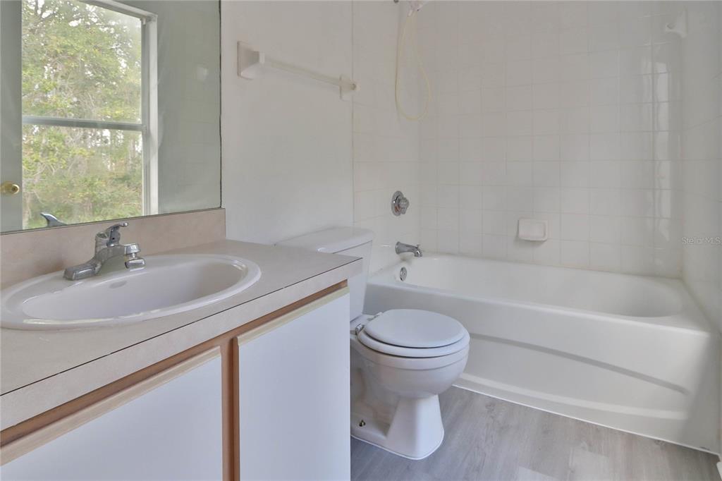 A bathroom features a vanity with a sink, a toilet, and a white tiled tub — 30205 SWINFORD LANE, WESLEY CHAPEL, FL